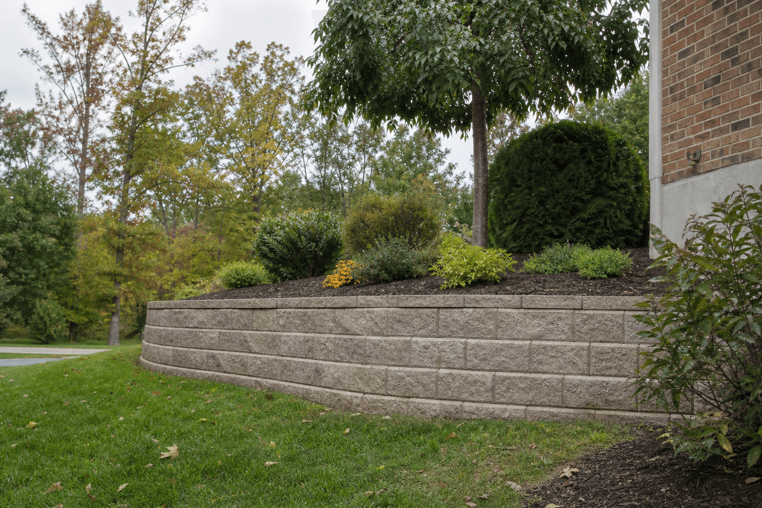 Illustrative landscaped block retaining wall beside shrubs and lawn in early autumn