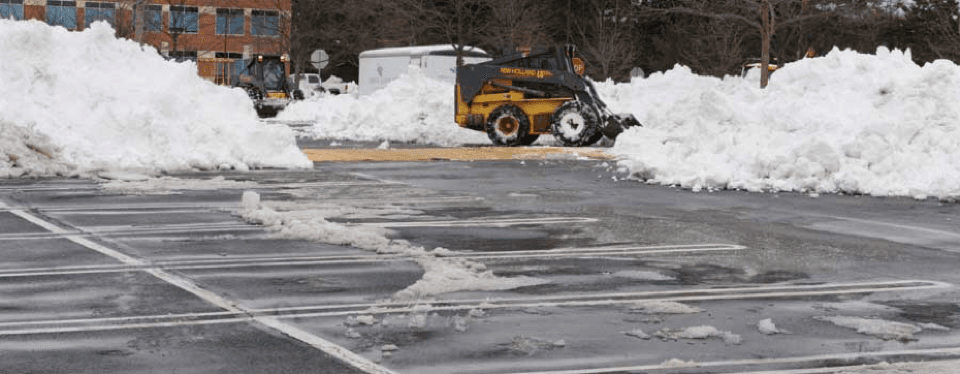 Skid steer clearing snow from a commercial parking lot