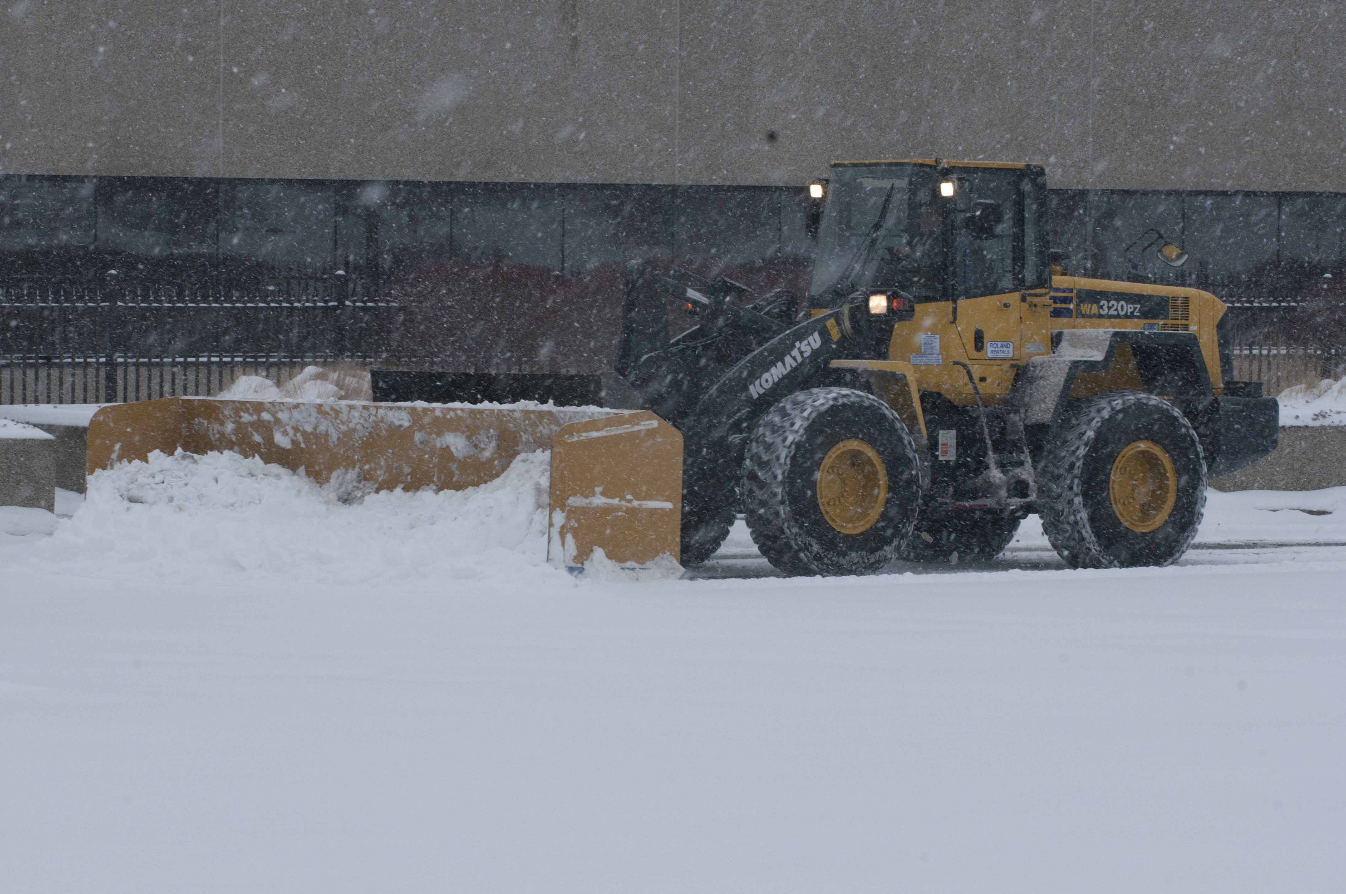 Front-end loader plowing snow from a commercial lot during a storm